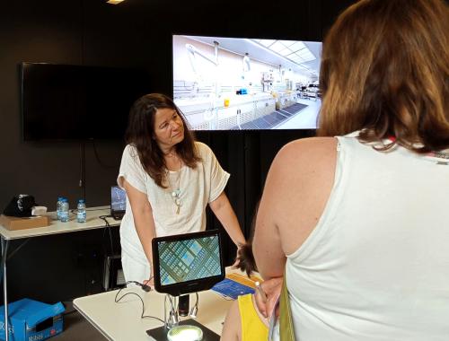 Mireia Bargalló amb microscopi i televisió mostrant una sala blanca al taller "Què s'amaga dins d'un xip?" a la Festa de la Ciència 2025 de Barcelona