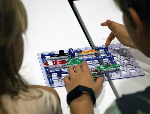 Espalda de dos niños jugando con un circuito electrónico en taller de Nit de la Recerca