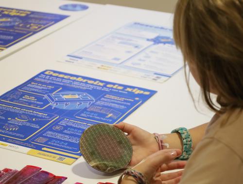 Niña tocando una oblea procesada, con un póster de divulgación sobre la mesa, en un taller en CosmoCaixa