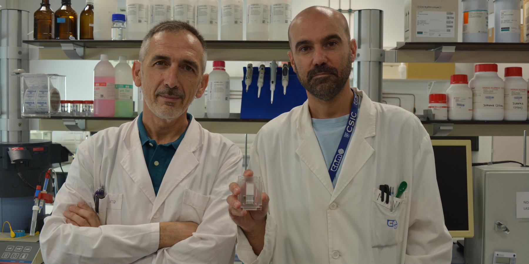 Los investigadores César Fernández-Sánchez y Manuel Gutiérrez-Capitán posan en el laboratorio con el dispositivo de papel para detección de enfermedades pulmonares