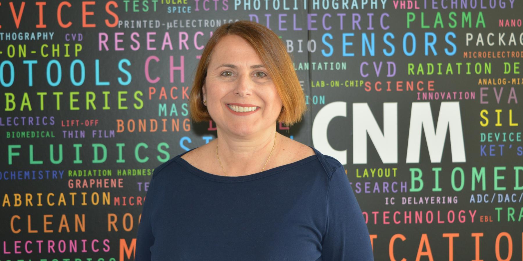 La nueva gerente del IMB-CNM Mari Carmen Porto sobre fondo negro con letras de colores en el IMB-CNM