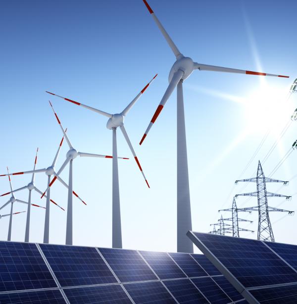 Montaje de paneles solares, palas eólicas y red eléctrica sobre cielo azul y despejado. iStock